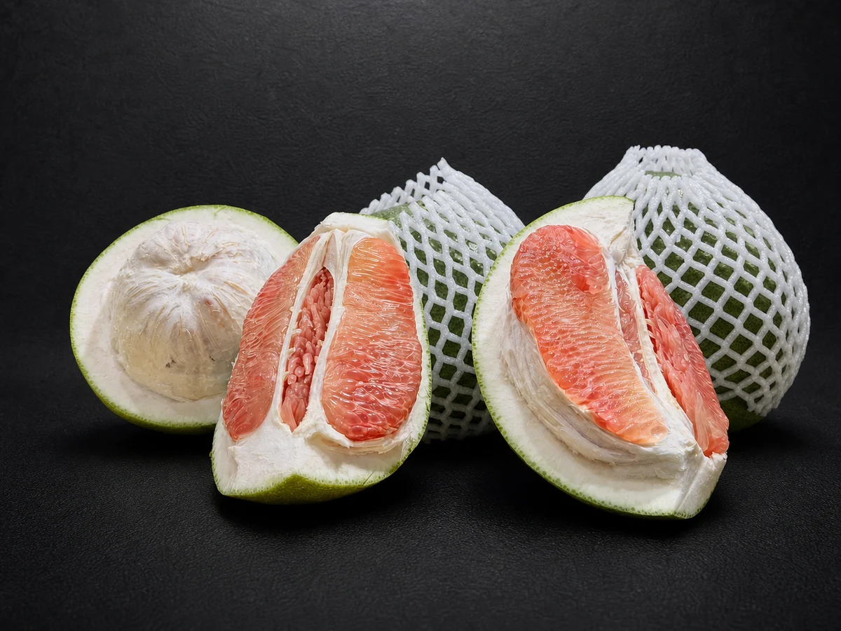 ネットに包まれた緑色のザボンと、半分に切った断面。厚い白い皮とピンク色の果肉