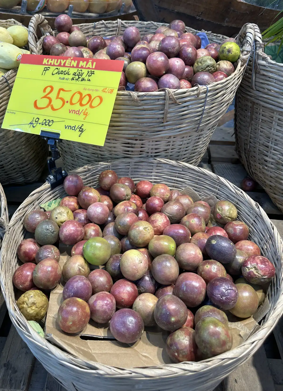 売り場のかごに並ぶ赤紫色のパッションフルーツと、「KHUYẾN MÃI」「FF Chanh dây YG」「35,000 VND/kg」と書かれた値札