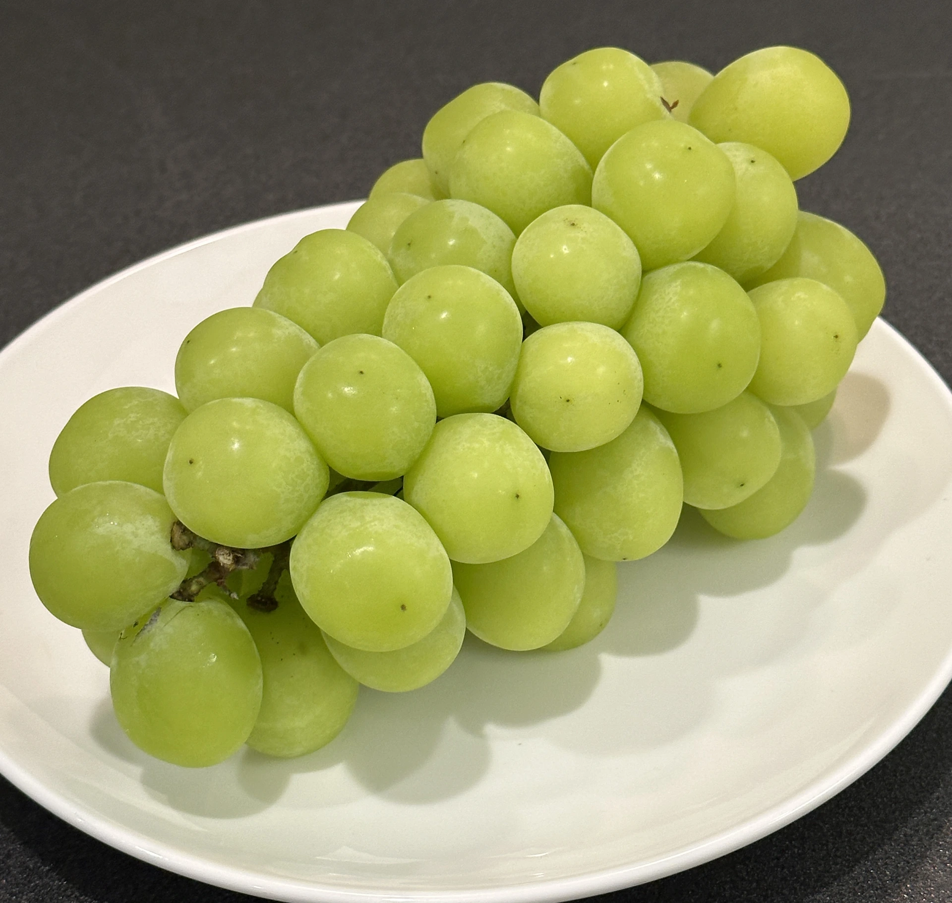 白い皿に載せた緑色のぶどうの房